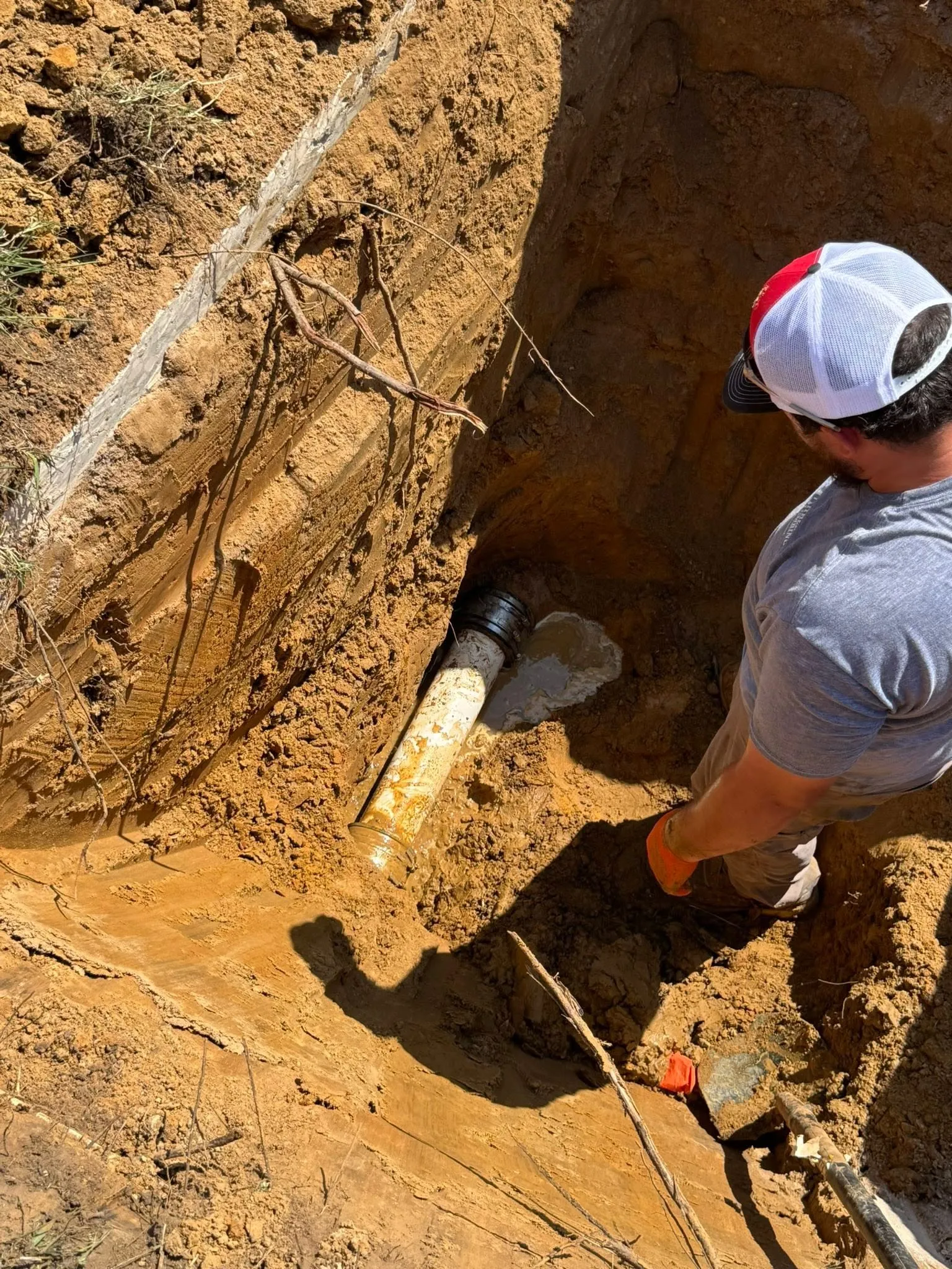 Pither technician standing in a deep excavation beside an exposed sewer pipe and its rubber coupling